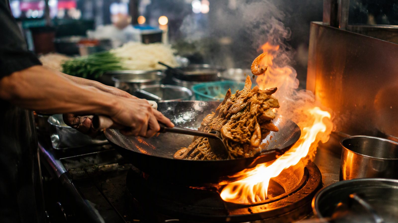 Un vendeur ambulant en train de faire frire du char kway teow dans un wok enflammé, à George Town, Penang, en Malaisie